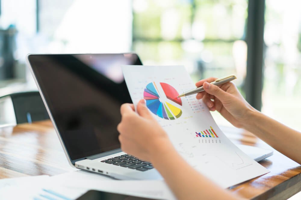 A businesswoman's hands holding a pen and paper while a laptop sits on a table.