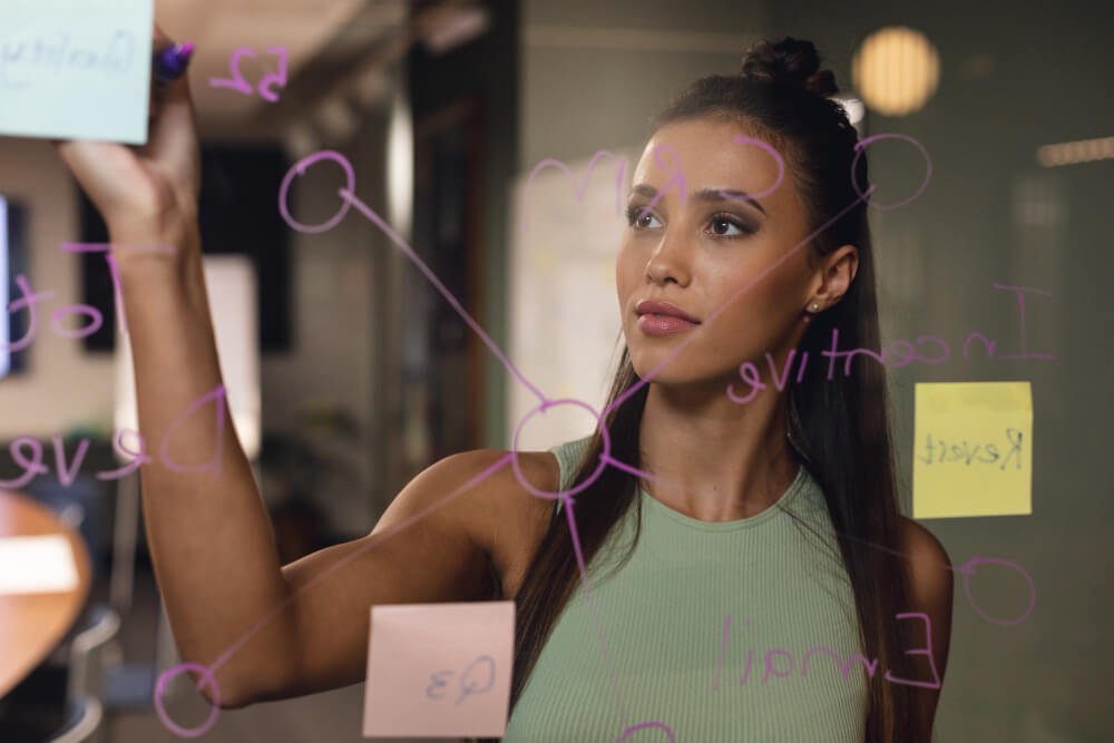 Female professional using sticky notes on a board in a workplace.