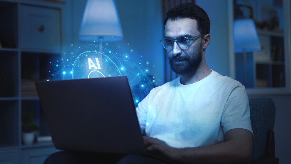 A bearded man wearing glasses is using a laptop displaying an AI logo.